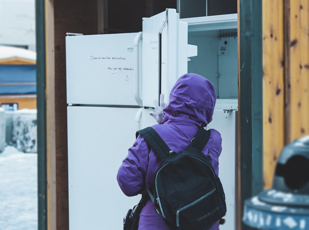person in purple hoodie standing near white top mount refrigerator