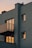 A modern apartment building with a minimalist design, featuring balconies and multiple windows reflecting a warm sunset light. The walls are painted in a muted gray color, and the scene is captured at dusk with a soft, ambient glow.