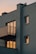 A modern apartment building with a minimalist design, featuring balconies and multiple windows reflecting a warm sunset light. The walls are painted in a muted gray color, and the scene is captured at dusk with a soft, ambient glow.