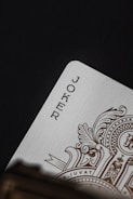 A close-up of a playing card, specifically the Joker card, featuring intricate gold designs on the edges and textured paper.