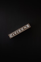 A rectangular box with the word 'CITIZENS' written in bold, decorative letters on its side, set against a dark background. The design is intricate, featuring patterns and metallic accents.