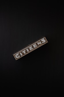 A rectangular box with the word 'CITIZENS' written in bold, decorative letters on its side, set against a dark background. The design is intricate, featuring patterns and metallic accents.