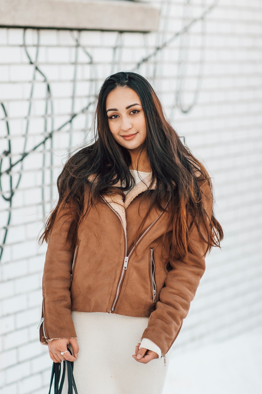 woman in brown leather jacket standing beside white wall