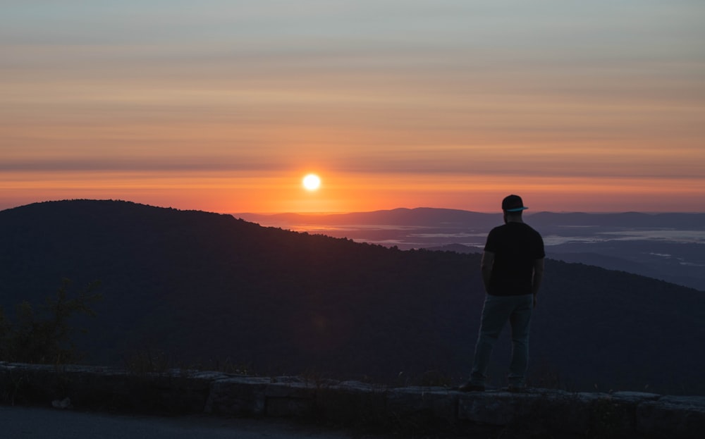 Silhouette eines Mannes, der während des Sonnenuntergangs auf dem Gipfel des Berges steht