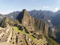 A breathtaking view of ancient ruins nestled high in the mountains, featuring stone structures and terraces with a backdrop of lush, green peaks and a clear sky.