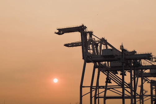 A large crane lifting heavy machinery at an industrial site during sunset.