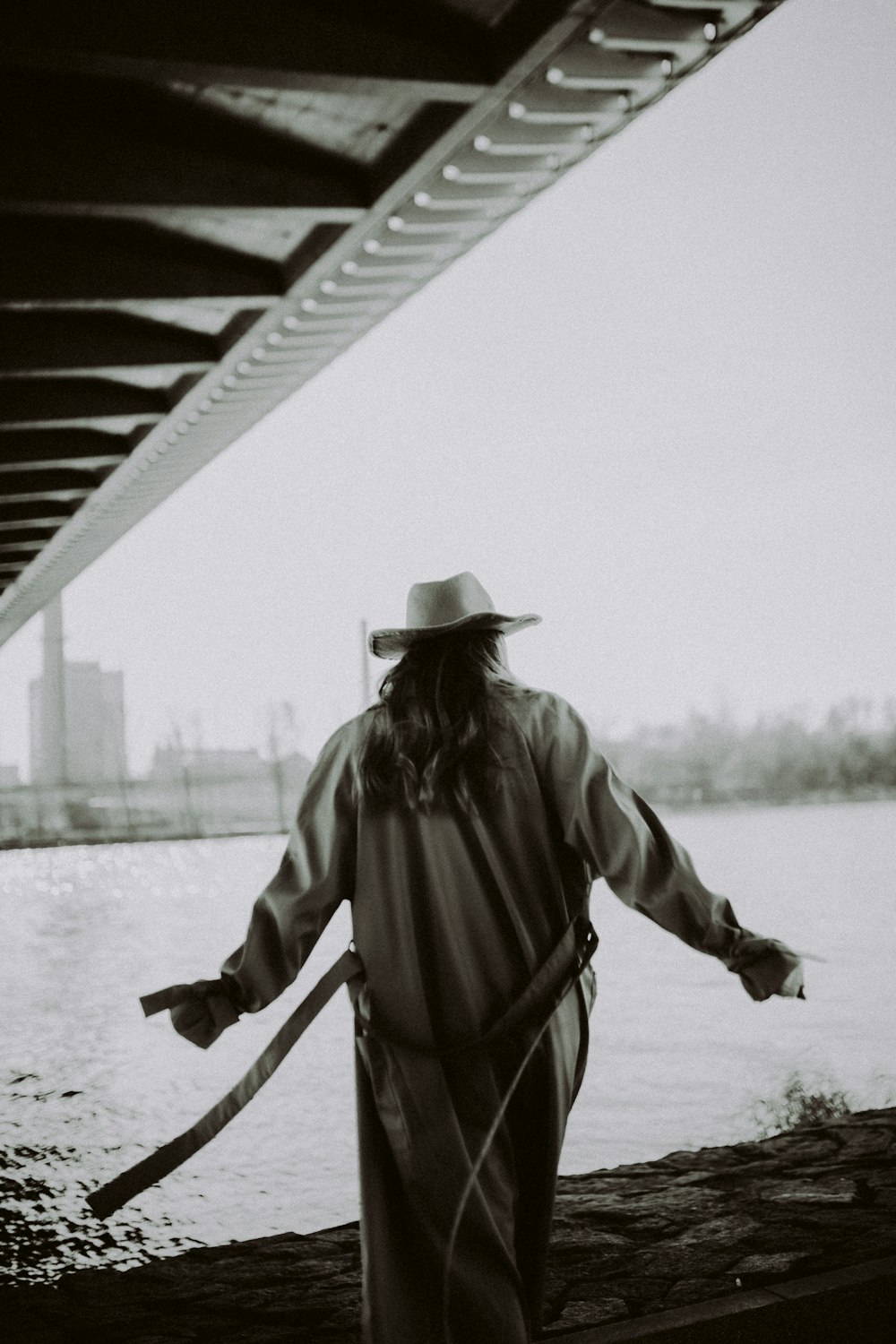 man in black cowboy hat and brown coat standing on bridge during daytime