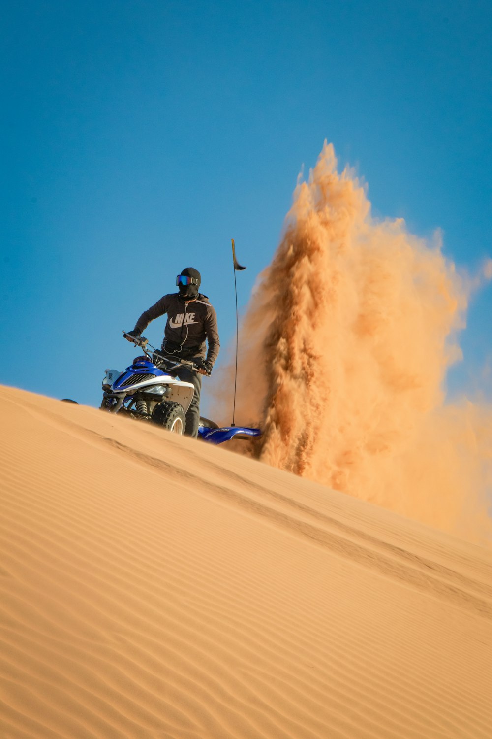 昼間、砂漠で青と白のモトクロスダートバイクに乗っている男
