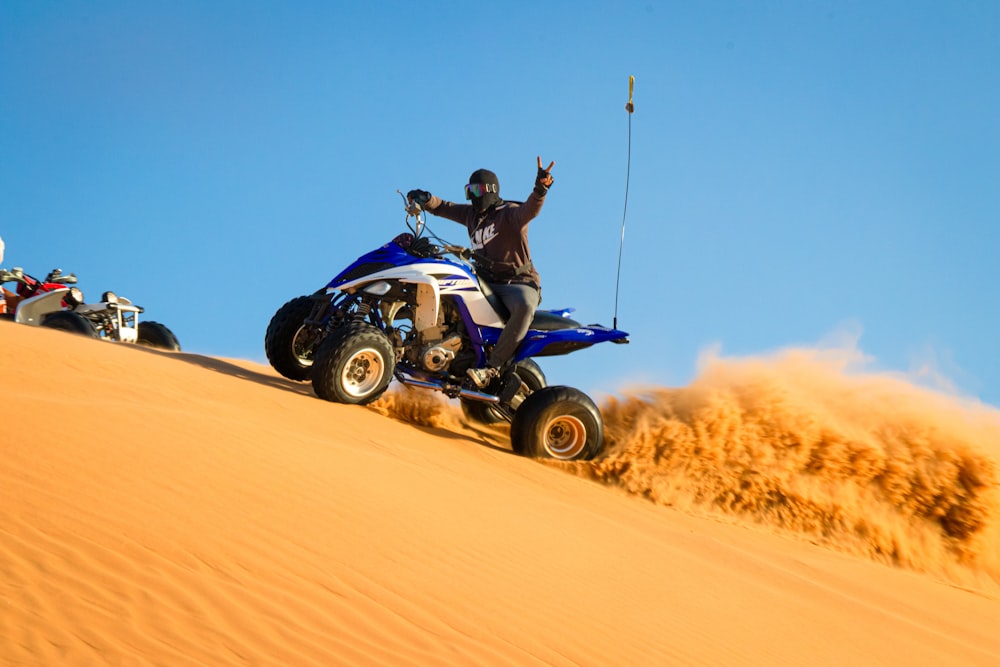 昼間の砂漠で黒と青のATVに乗っている男