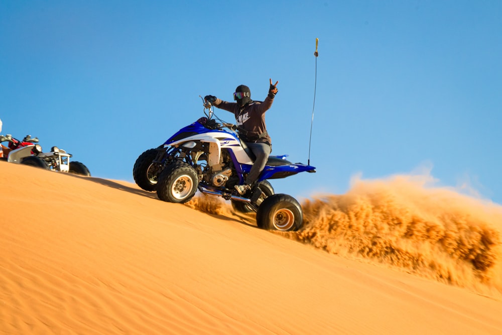 man riding on black and blue atv on desert during daytime