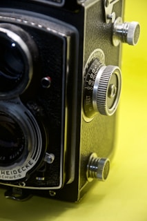 Close-up of a vintage film camera against a yellow backdrop, highlighting intricate details of the lens.