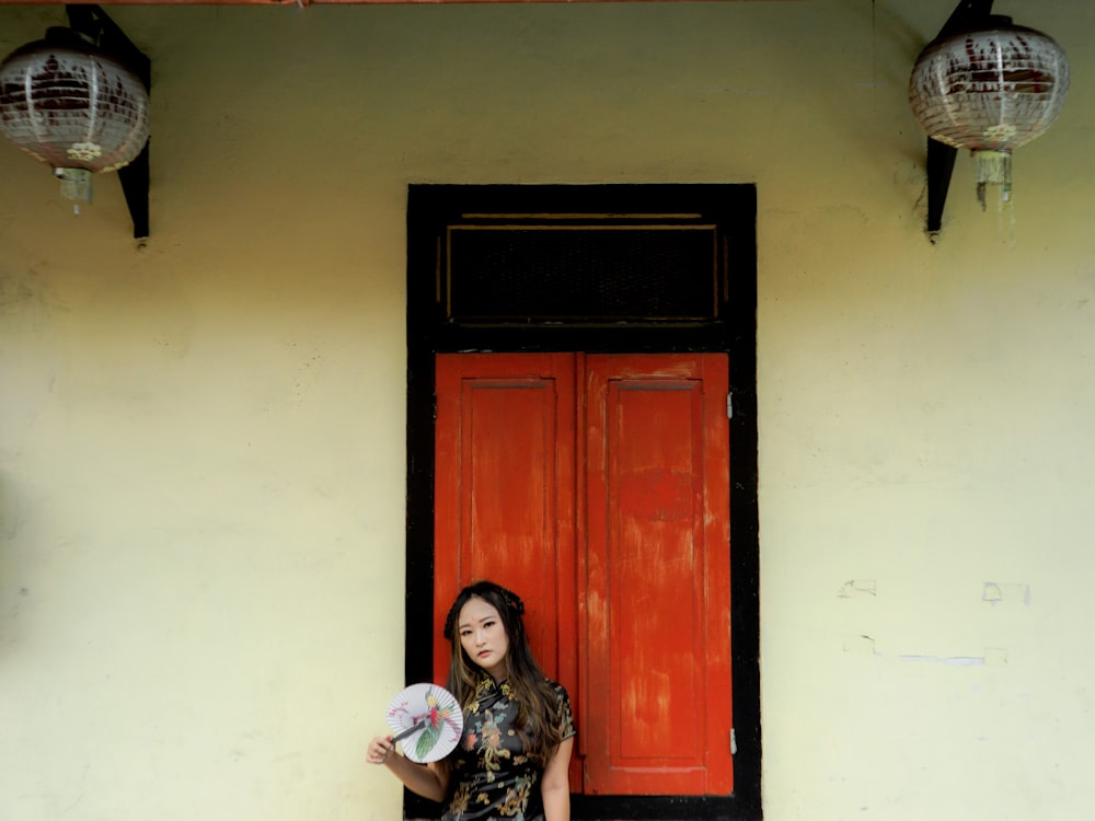 a woman holding a frisbee standing in front of a red door