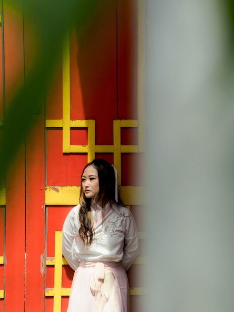 Woman in traditional Chinese dress standing in front of warm-toned wall, illustrating the cross-cultural fashion conversation between Asia and Europe