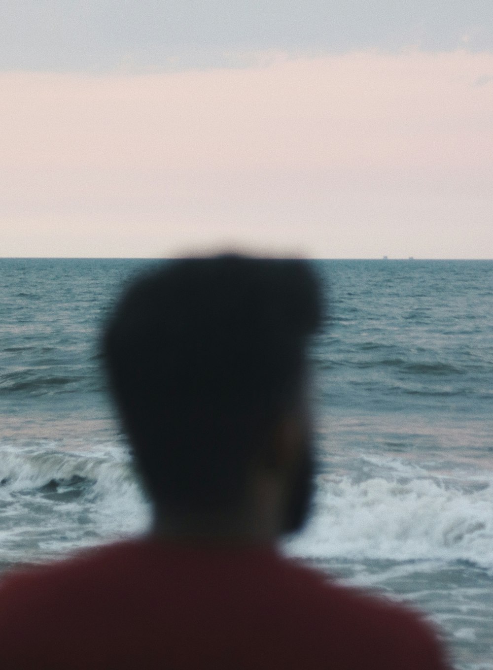 man in red shirt standing on sea shore during sunset