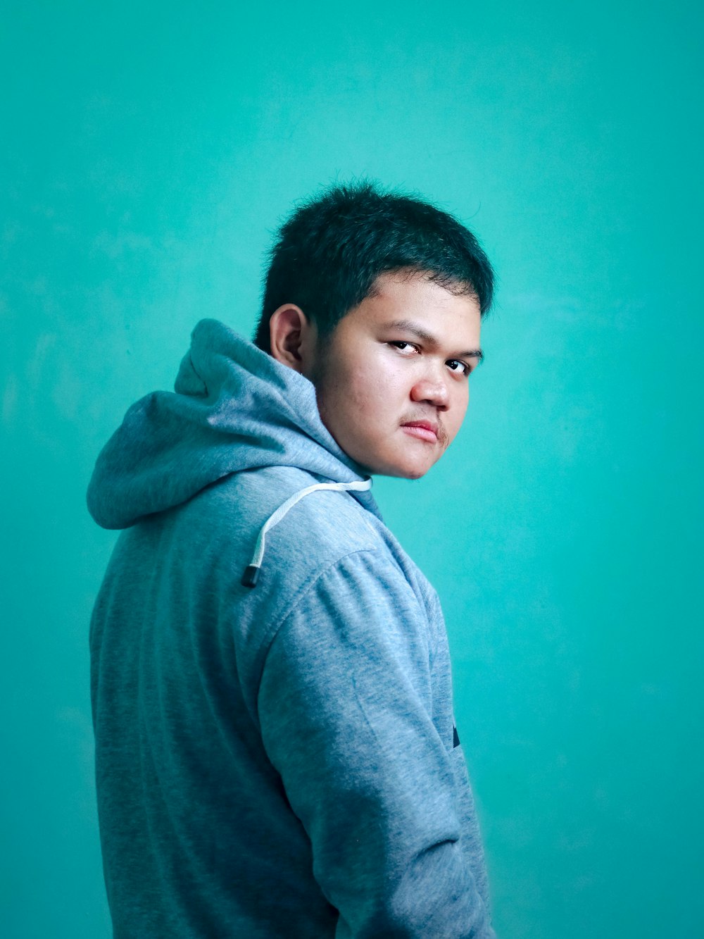 man in gray hoodie standing beside blue wall