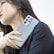 A person with long dark hair holding a sleek, modern smartphone. The phone is metallic with several camera lenses visible. The individual is dressed in a black outfit, and their gaze is directed away from the camera.