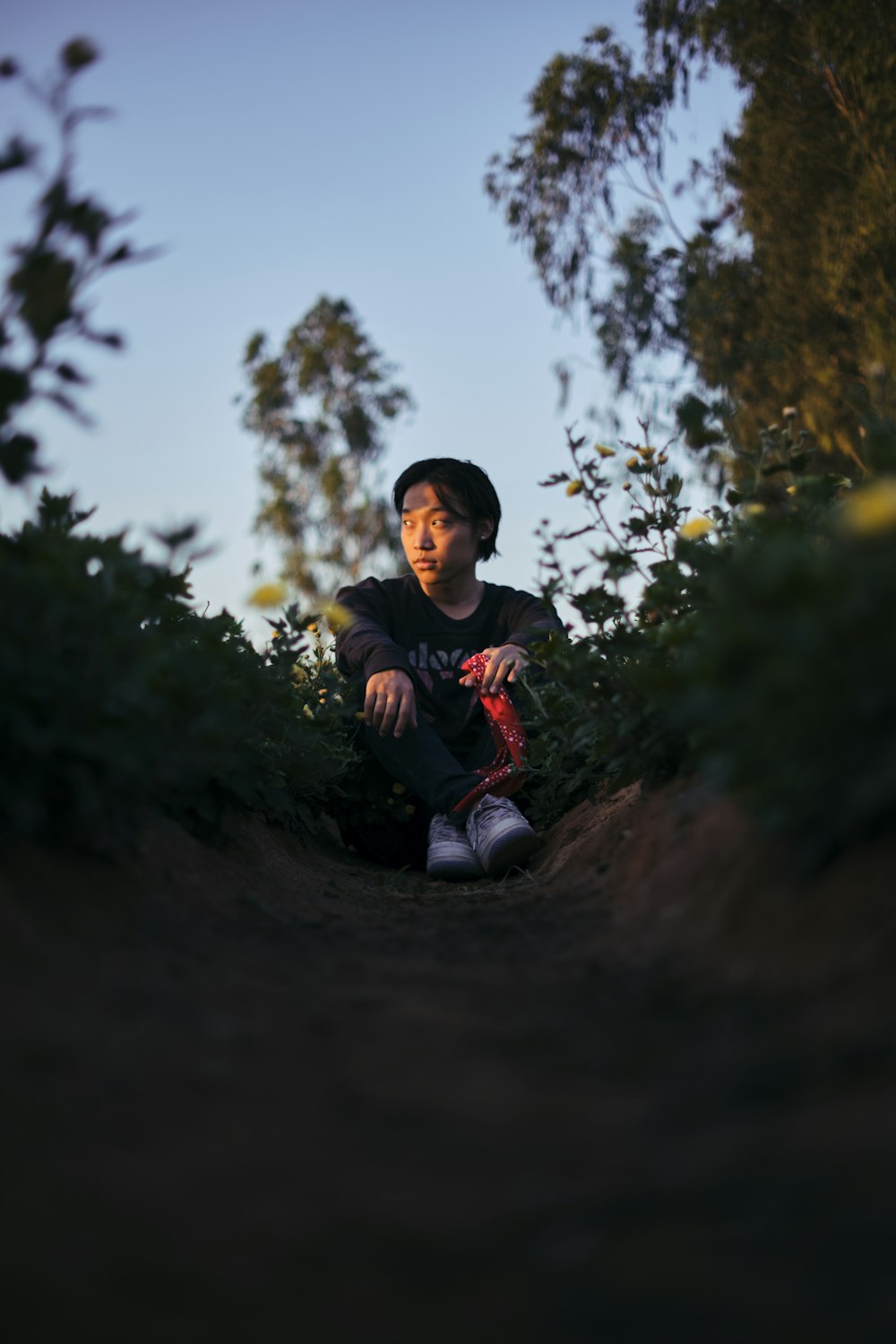 boy in red and black jacket sitting on brown rock during daytime