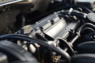 A close-up view of a car engine, showcasing various components such as hoses, wires, and the metal framework. The image is focused on the intricate details of the engine parts, highlighting the mechanical complexity.