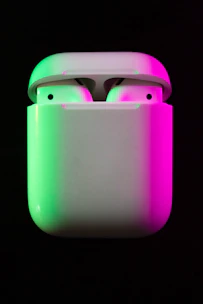 Close-up of a pair of wireless earbuds glowing softly against a black background.