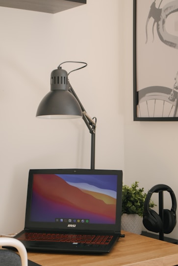 A minimalist workspace with sleek black and white decor, featuring a laptop, a plant, and soft natural light.