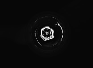 A high-resolution, wide-aspect image featuring a deep black background with subtle geometric blockchain lines and a faint central glow.