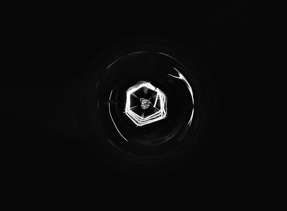 A high-resolution, wide-aspect image featuring a deep black background with subtle geometric blockchain lines and a faint central glow.