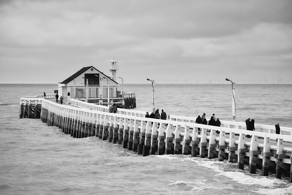 grayscale photo of people standing on wooden dock near body of water