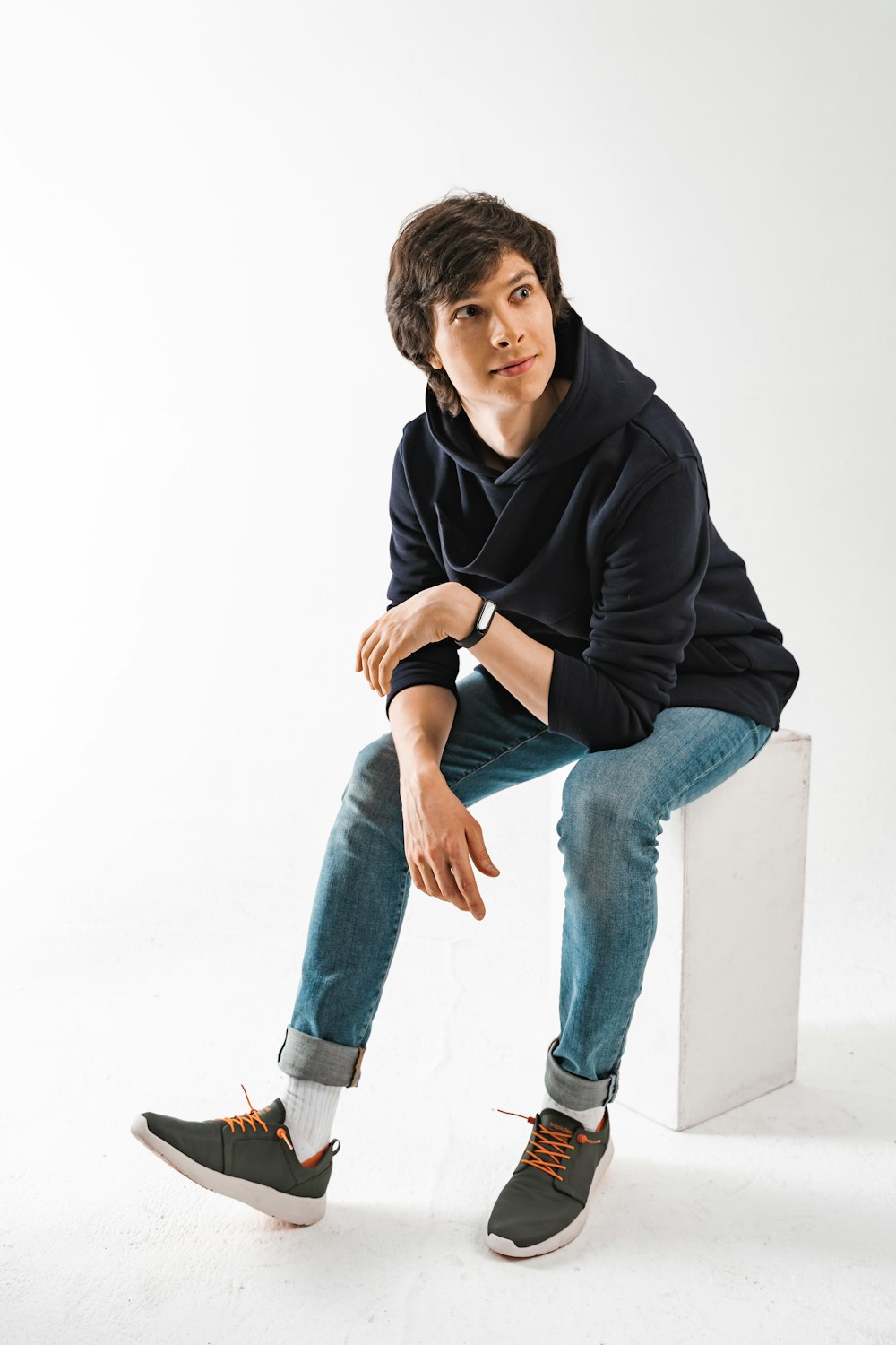 man in black hoodie and blue denim jeans sitting on white floor