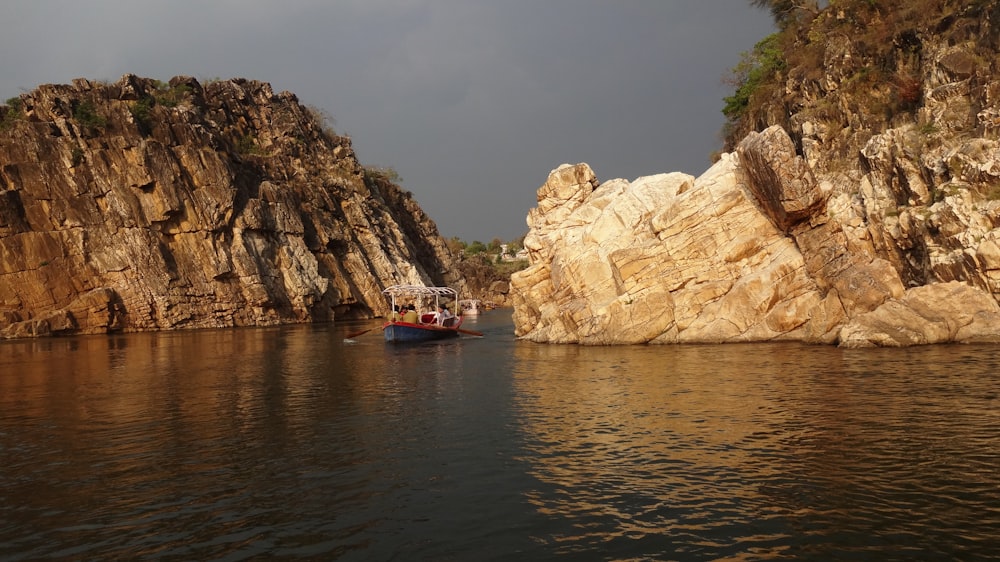 Bateau rouge sur un plan d’eau près d’une formation rocheuse brune pendant la journée