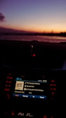 A car dashboard with an infotainment screen displaying music information, showing a song by Damien Rice during twilight. The background features a serene sunset over a body of water, with a gradient of colors from orange to purple in the sky.