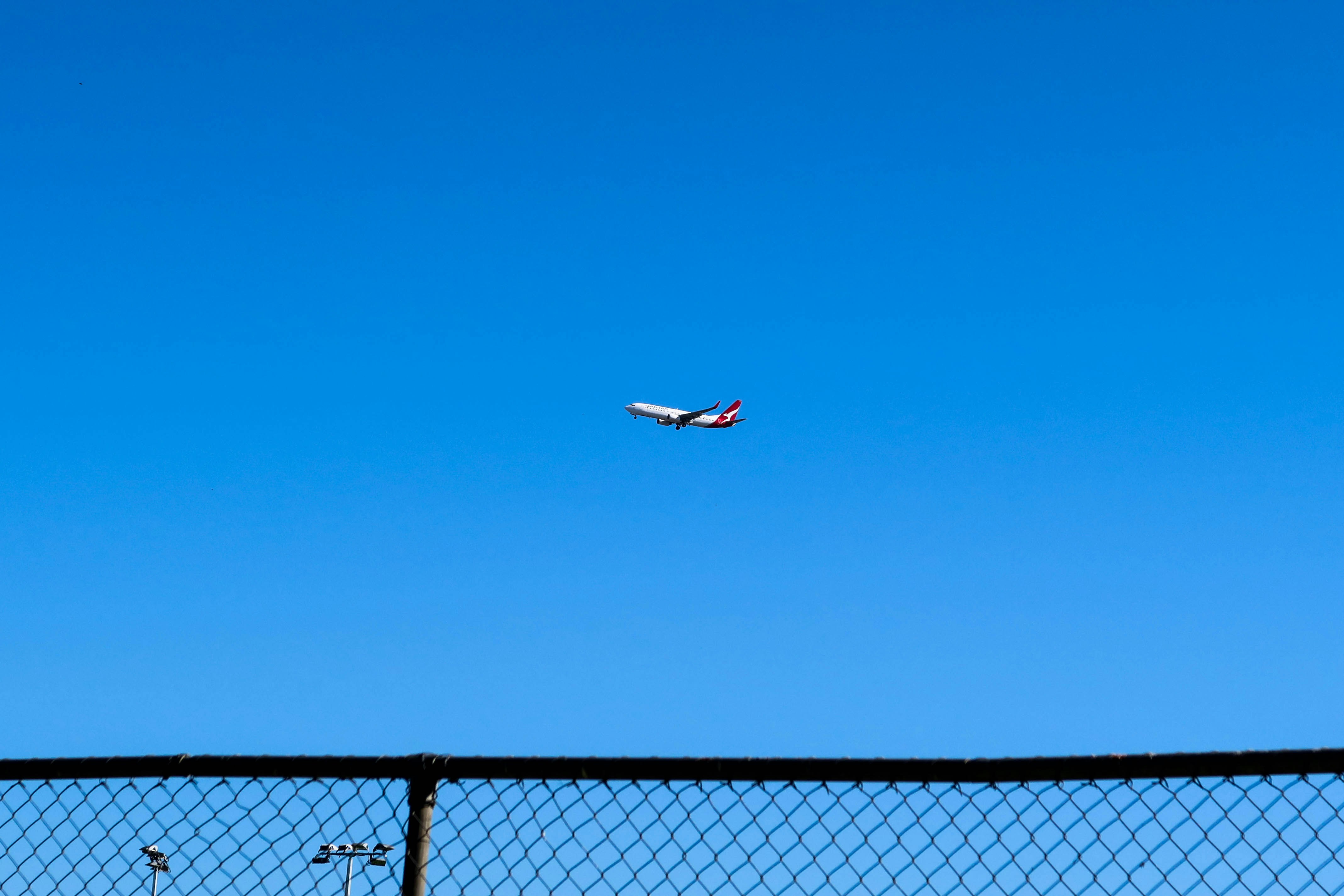 white and red airplane flying over black metal fence during daytime