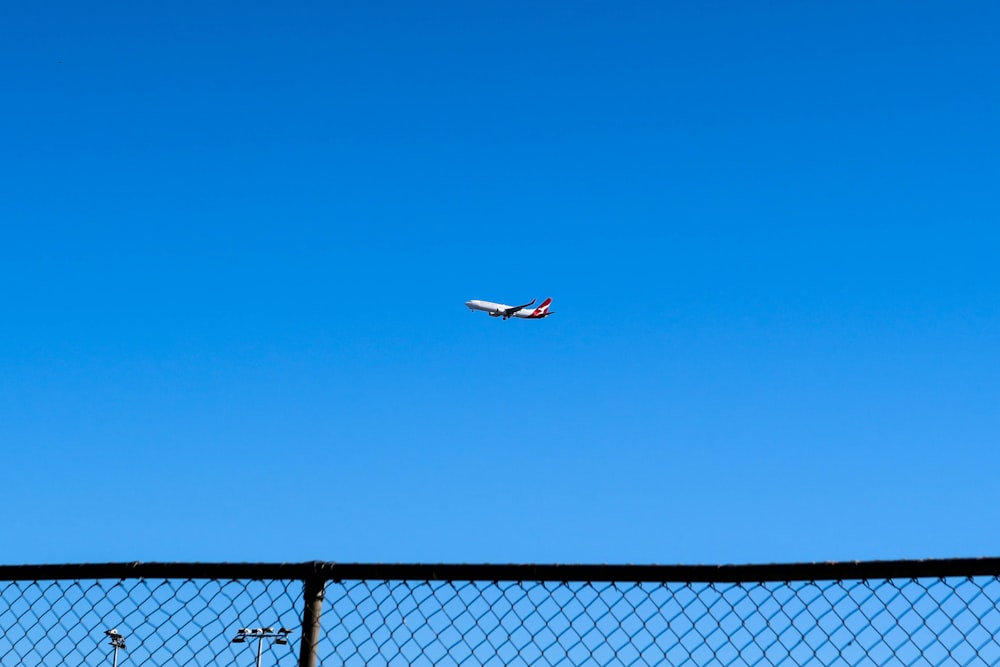 white and red airplane flying over black metal fence during daytime