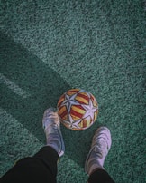 Children playing soccer barefoot transitioning to wearing donated shoes on a dusty field.