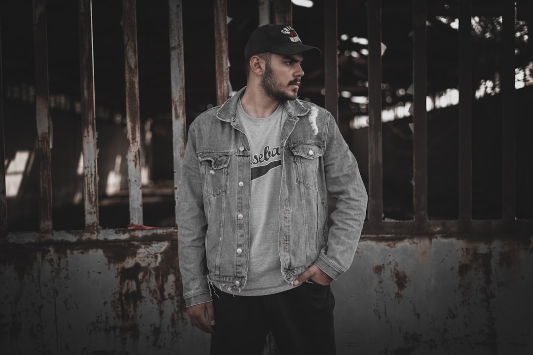 man in gray denim jacket and black pants standing near brown wooden door