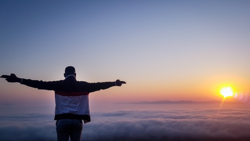 man in white shirt and black pants standing on top of mountain during sunset