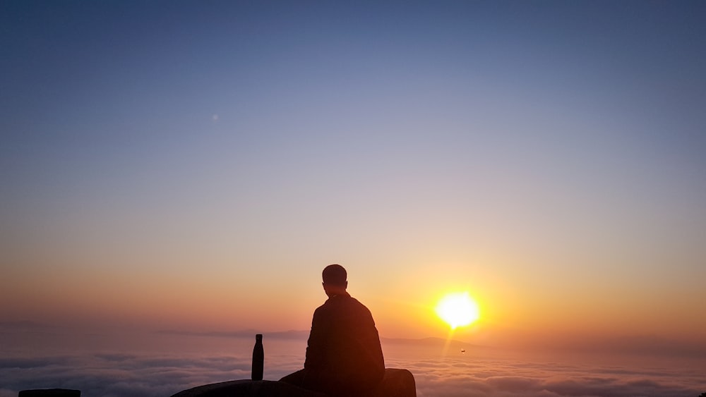 silhouette of man sitting on rock during sunset