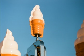 A cheerful ice cream cone character holding a handwritten note that says 'Contact Us' in bright colors.
