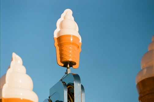 A cheerful ice cream cone character holding a handwritten note that says 'Contact Us' in bright colors.