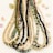 Multiple strands of colorful beads are arranged neatly, featuring a variety of bead types including gold, black, green, and cream hues. Small, decorative shells and stones are scattered around the beads on a light background.