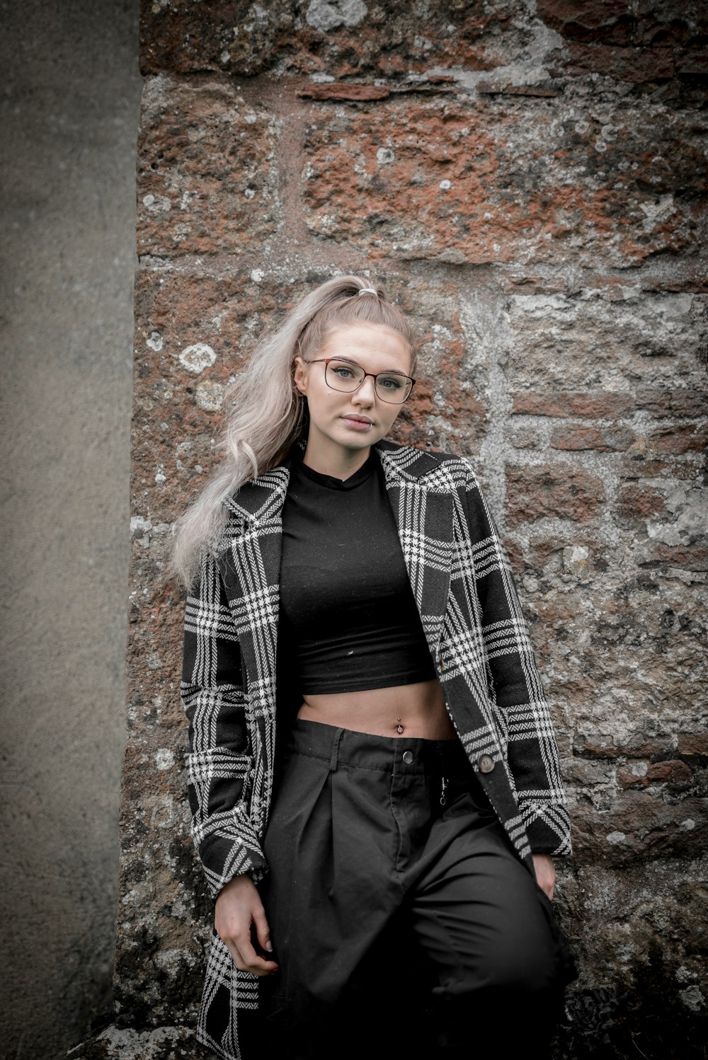 woman in black and white plaid long sleeve shirt leaning on brown brick wall