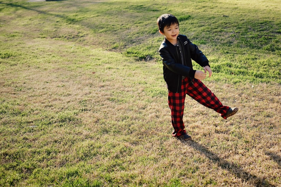 boy in black jacket and red pants standing on green grass field during daytime