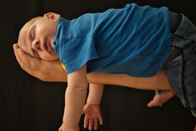baby in blue shirt lying on brown wooden floor