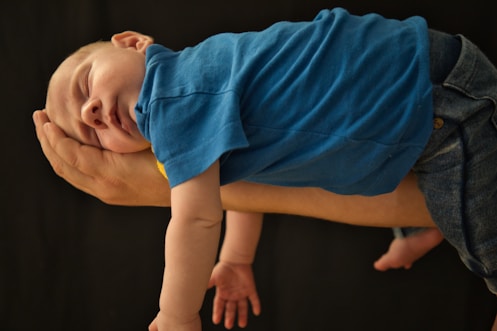 baby in blue shirt lying on brown wooden floor