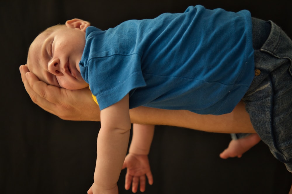 baby in blue shirt lying on brown wooden floor
