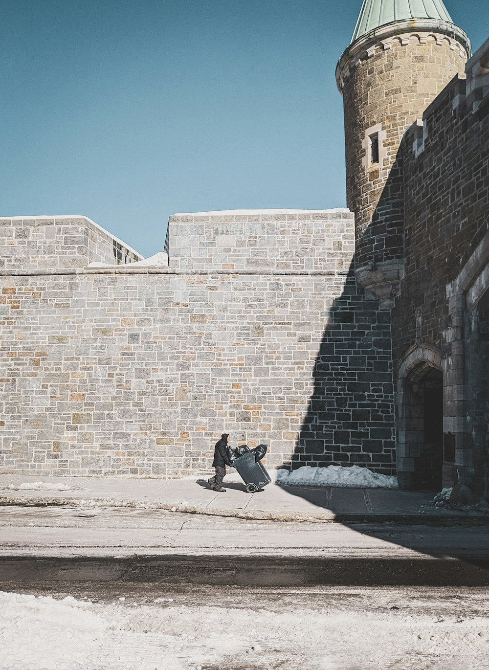 man in black jacket and black pants sitting on concrete bench beside brick wall during daytime