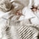 A partially knitted sweater made with cream-colored yarn is placed on a white surface. Next to it, there is a ball of yarn, a pair of small metallic scissors with an ornate handle, and a pair of sunglasses.