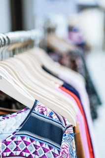 A collection of colorful clothes neatly arranged on wooden hangers displayed on a clothing rack. The garments feature various patterns and fabrics, showcasing a variety of styles.