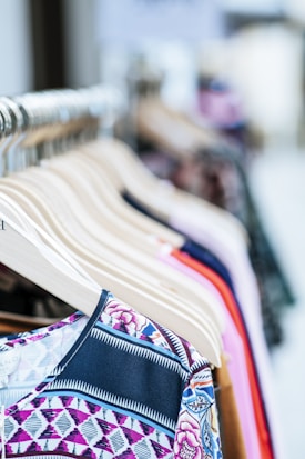 A collection of colorful clothes neatly arranged on wooden hangers displayed on a clothing rack. The garments feature various patterns and fabrics, showcasing a variety of styles.