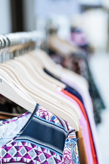 A collection of colorful clothes neatly arranged on wooden hangers displayed on a clothing rack. The garments feature various patterns and fabrics, showcasing a variety of styles.