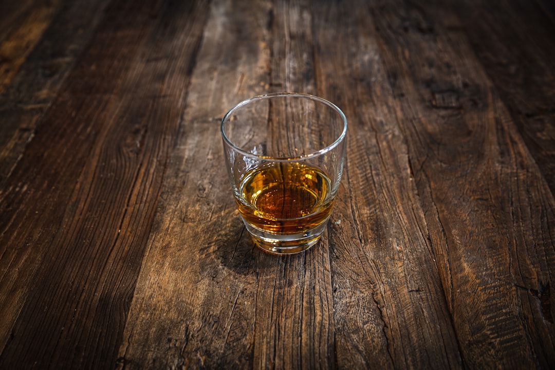 clear shot glass with brown liquid, Whiskey neat in glass on wood table.
